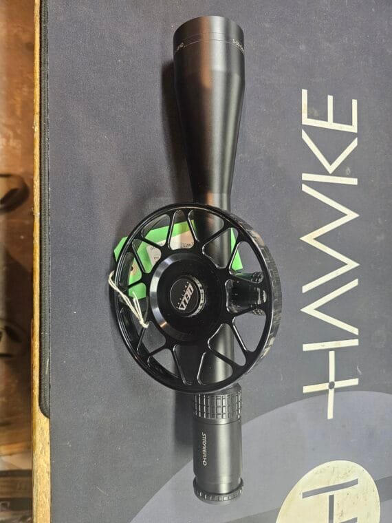 Black Hawke optics scope and fishing reel positioned on a surface with branding.