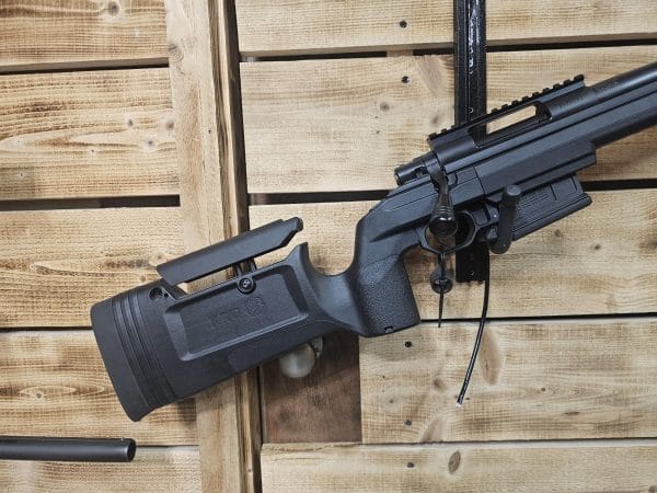 Black air gun with a tactical stock mounted on a wooden wall background.
