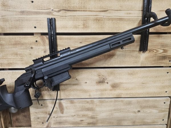 Black air gun with a long barrel and a mounted scope displayed against a wooden background.