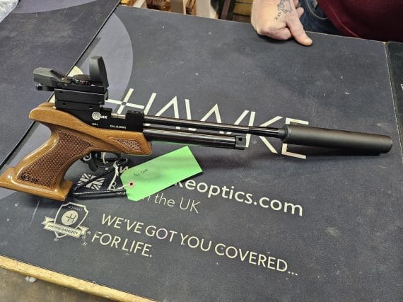 Air gun featuring a wooden stock, a scope, and a silencer on a display surface.