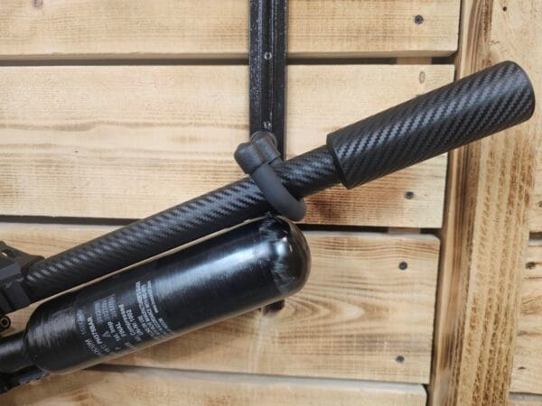 Close-up of a carbon fiber air gun barrel attached to an air cylinder on a wooden surface.