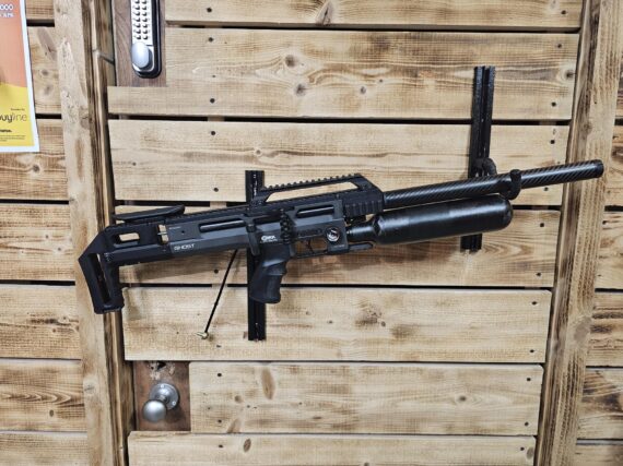 Black air gun with a sleek design mounted on a wooden wall in a shooting range.